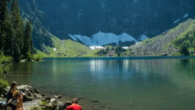 A panoramic view of snow-capped mountains reflecting on a serene alpine lake under a clear blue sky.