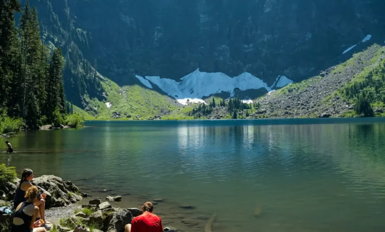 A panoramic view of snow-capped mountains reflecting on a serene alpine lake under a clear blue sky.