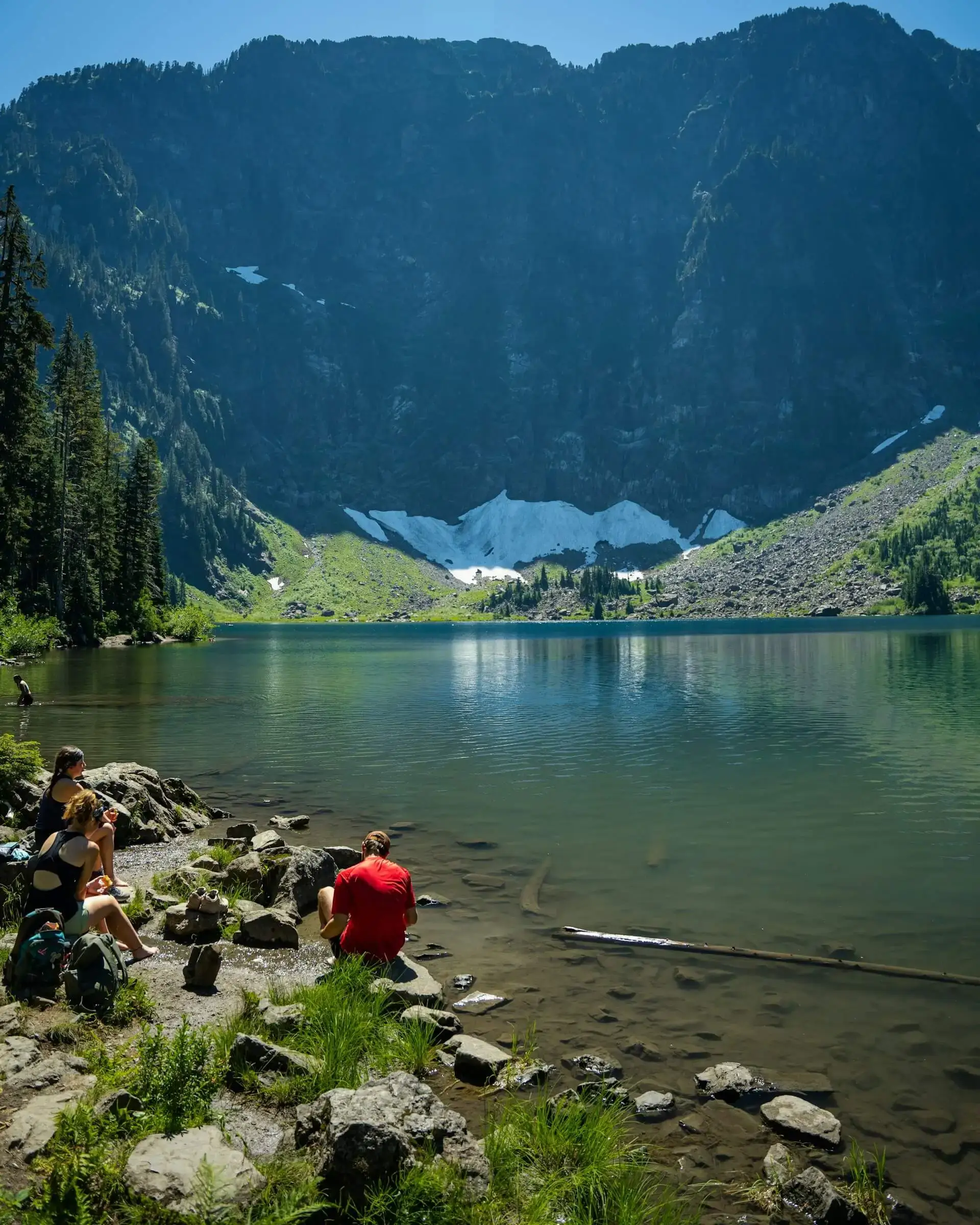 A panoramic view of snow-capped mountains reflecting on a serene alpine lake under a clear blue sky.