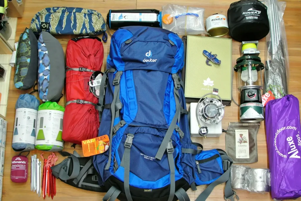 Essential packing items laid out for an outdoor adventure trip, including backpack, boots, and camping gear