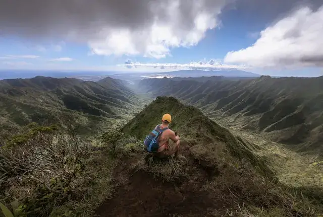 A solitary hiker traverses a narrow mountain trail enveloped in mist, surrounded by towering peaks and untouched wilderness.